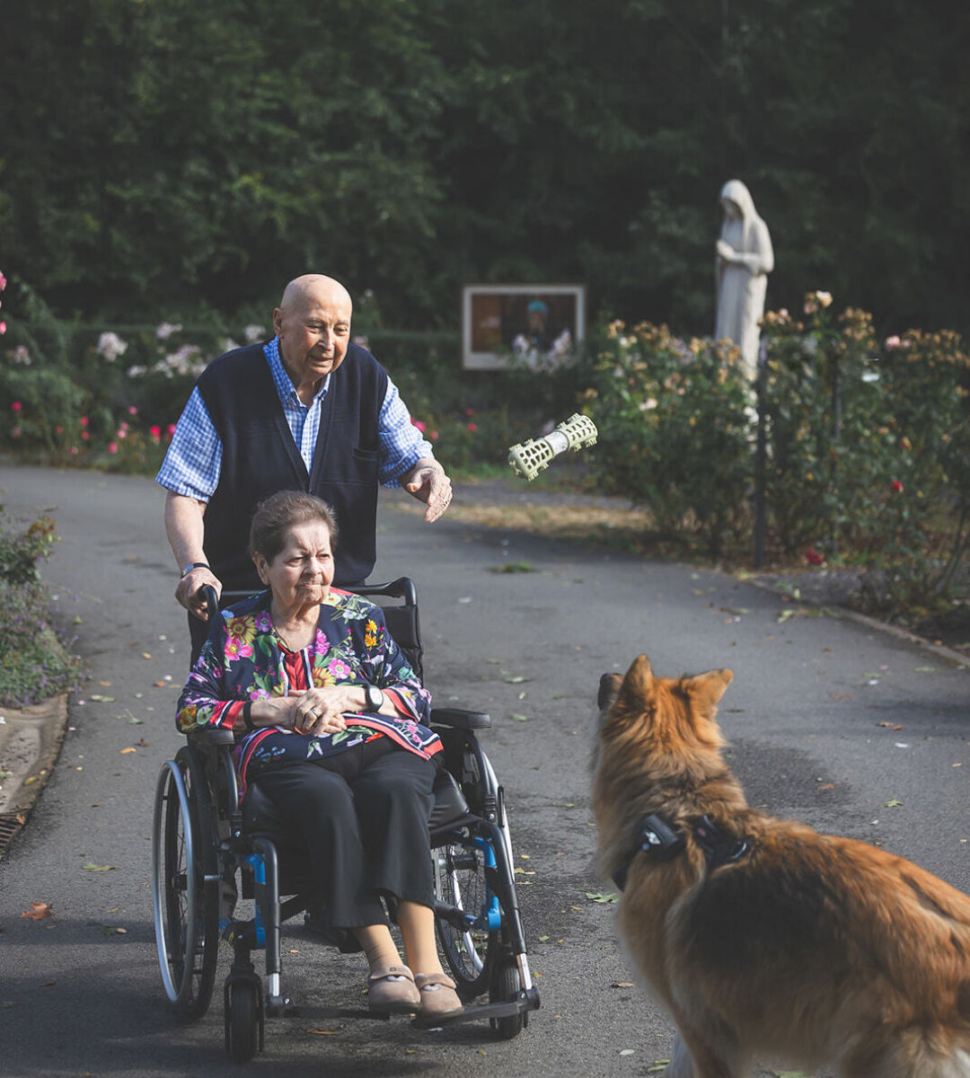 mannelijke zorgvrager en vrouwelijke zorgvrager in rolstoel spelen buiten met hond